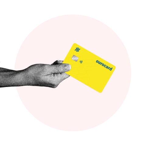 mão segurando um cartão de cŕedito ourocard, ao fundo um circulo rosa claro